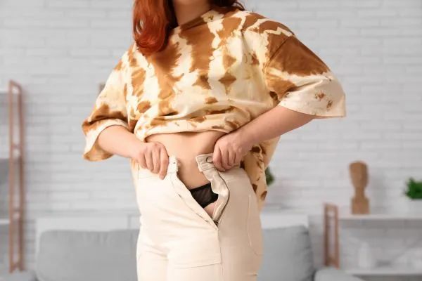 Image of woman trying to do her trousers up after pregnancy weight gain Southall