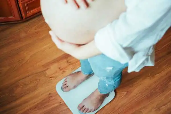 Image of woman weighing herself and experiencing weight gain through pregnancy Southall